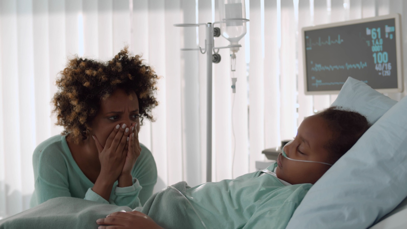 Upset young african woman crying sitting near little daughter sleeping in bed at hospital. 